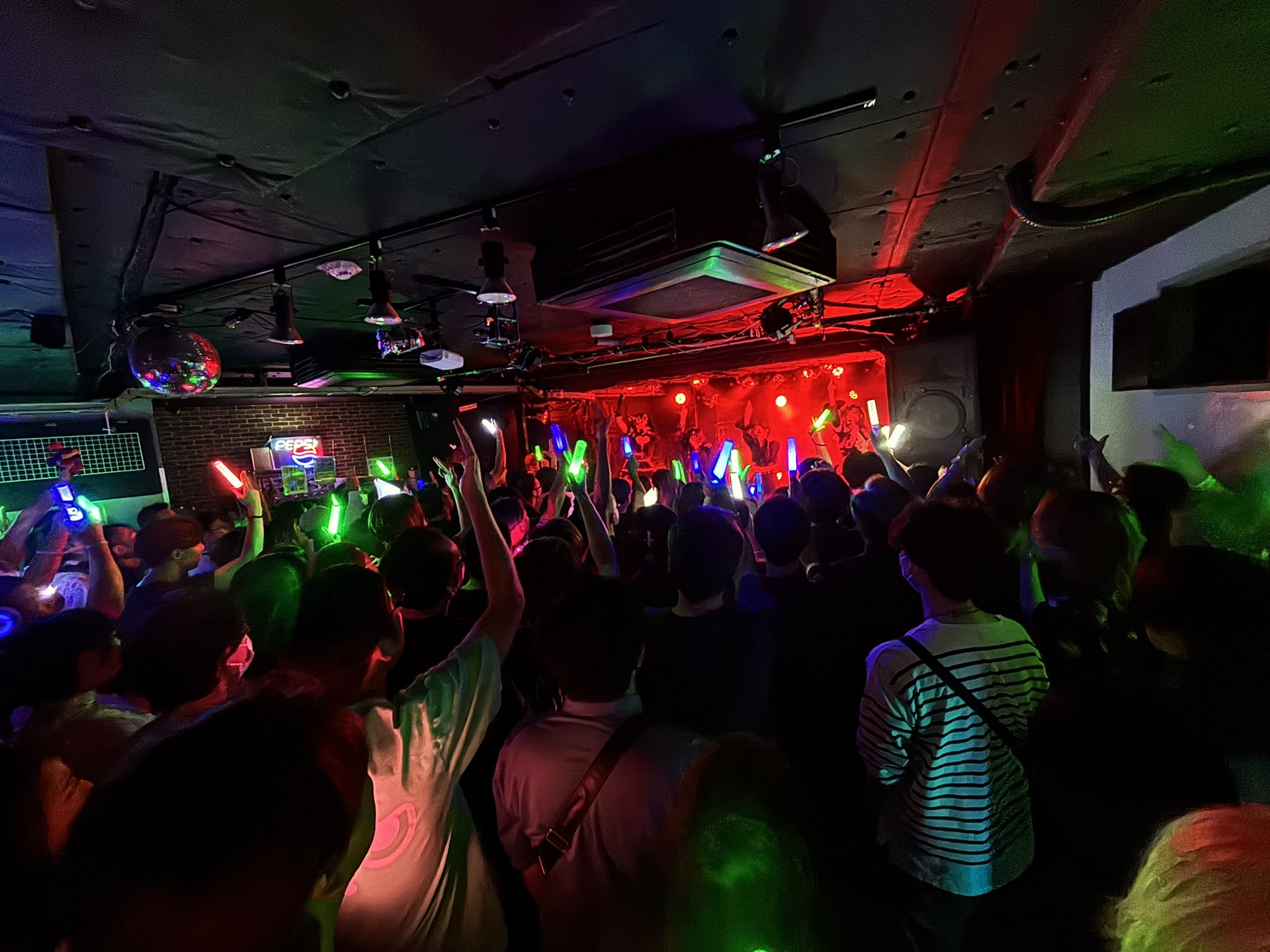 CHAAKLiLYのライブ。赤い照明のステージに向かい、大勢の観客が色とりどりのペンライトを掲げている
